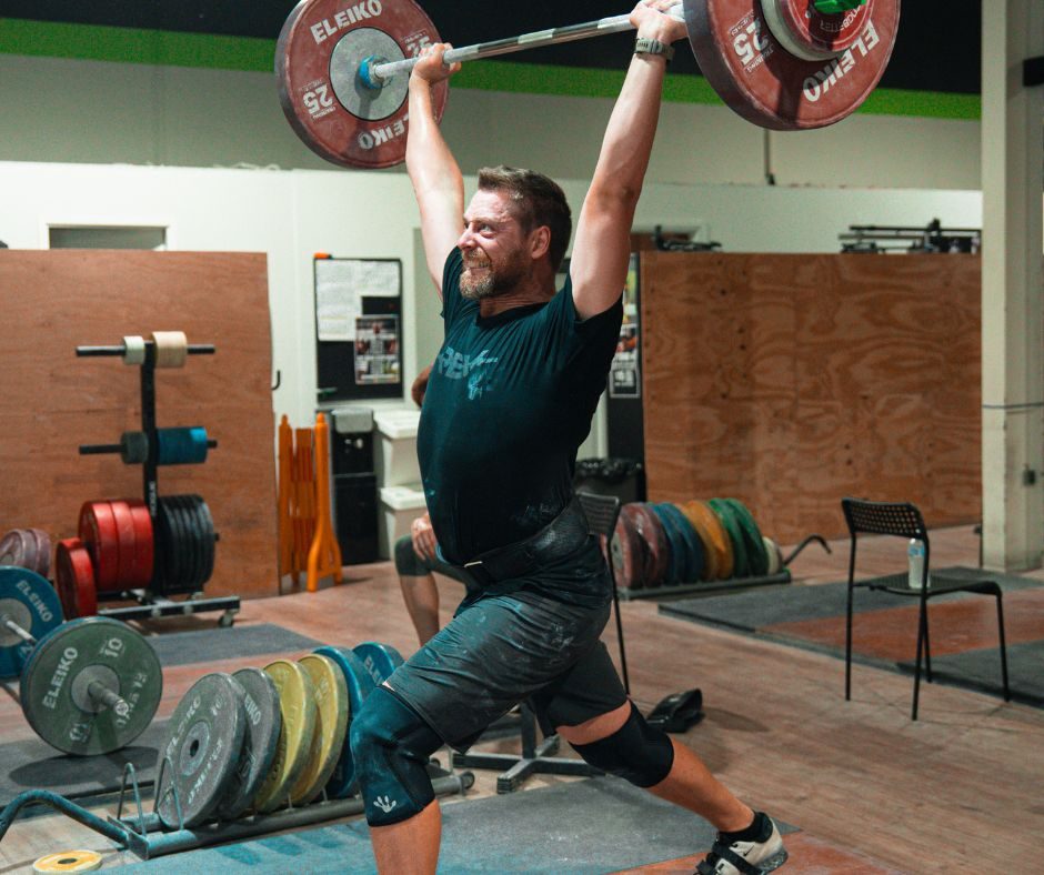 A Rev lifter holds a barbell overhead in a split jerk